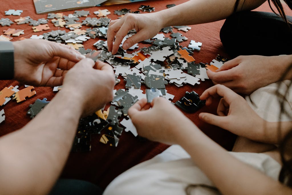 Close-up of multiple hands working together to solve a puzzle on a table indoors.